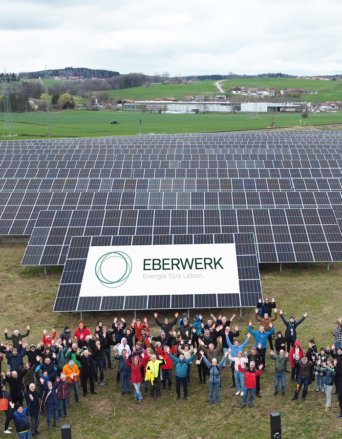 Viele an dem Solarpark Oberlaufing beteiligten Menschen stehen vor dem Solarpark und feiern die Energiewende